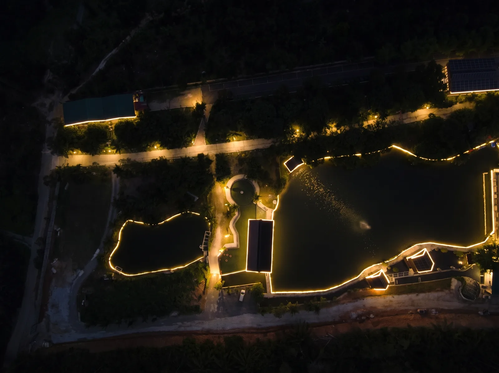 The heart of the farm from straight above at night: the lake and the pond traced in warm light, the chalet roofs outlined