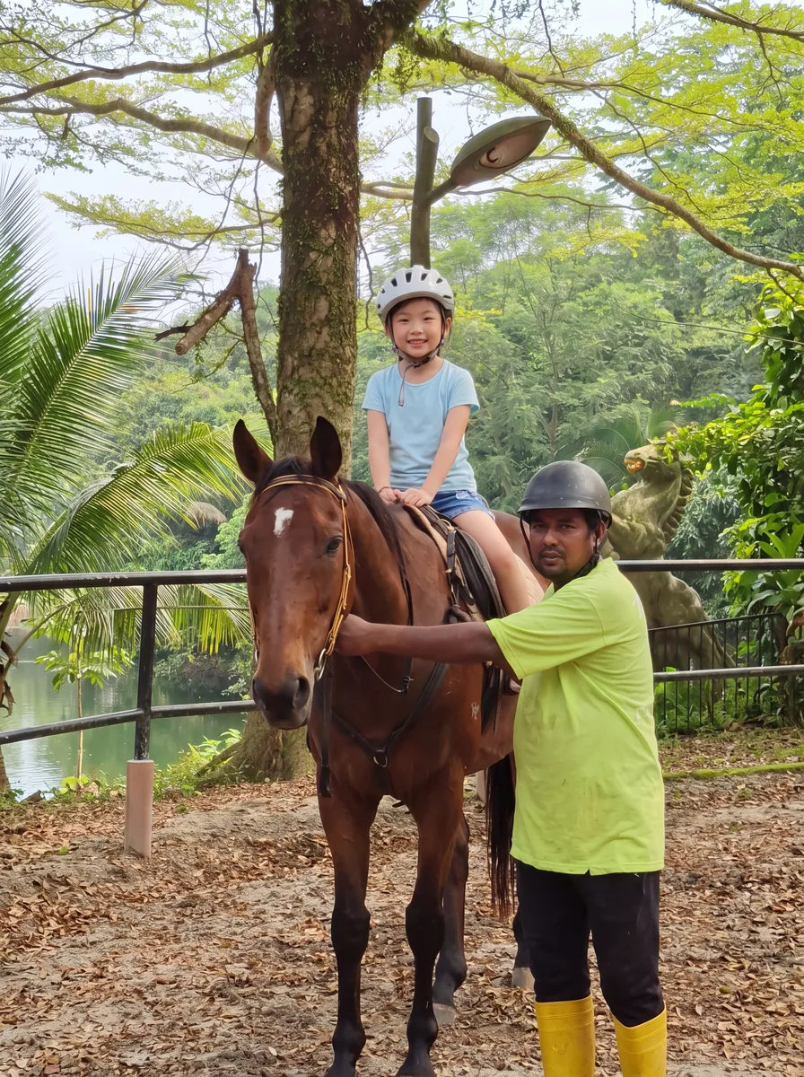 A girl in a riding helmet on the horse, the caretaker holding the reins