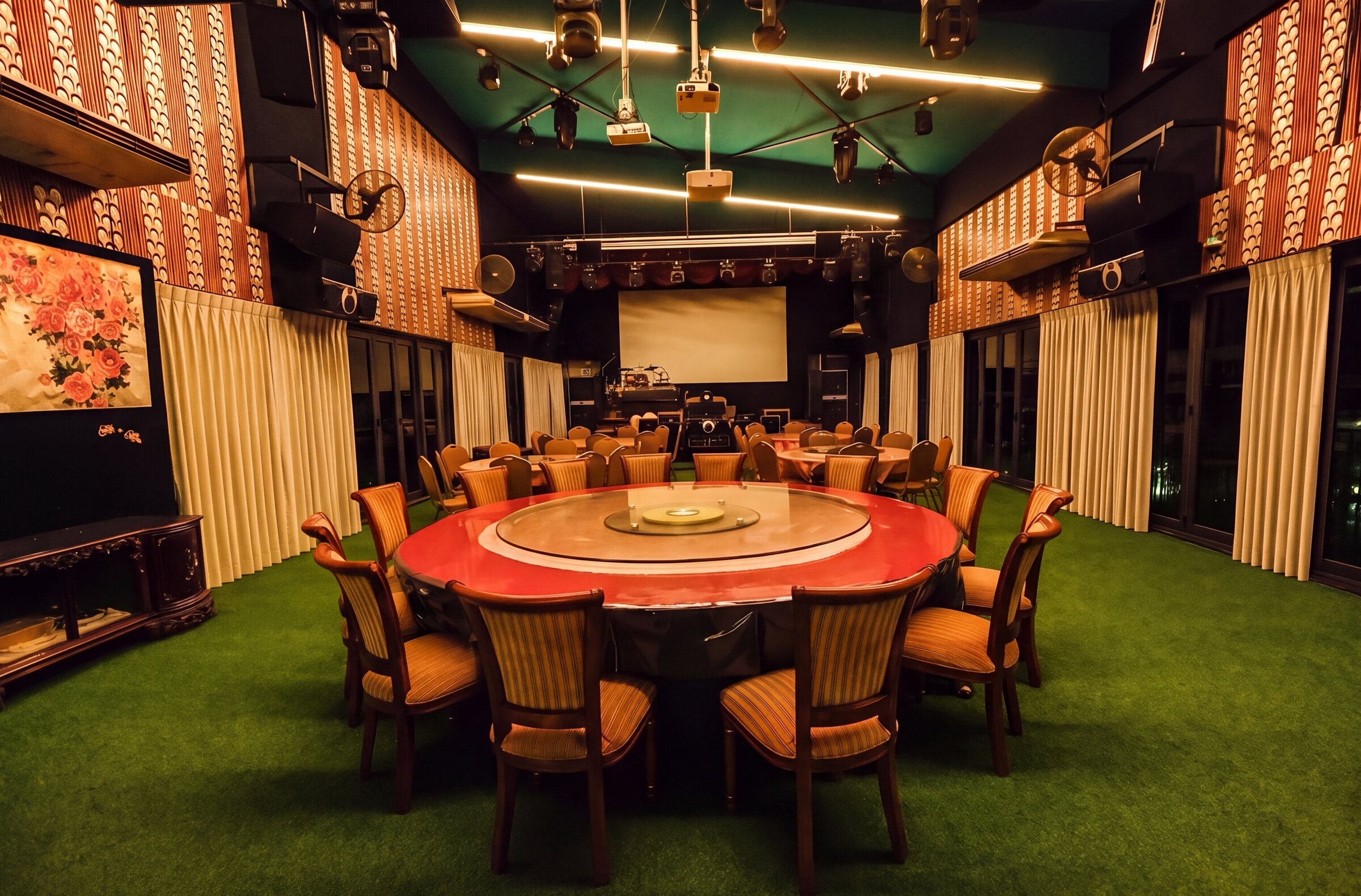Emerald Hall in light mode — warm lighting on a round dining table facing the stage and projection screen