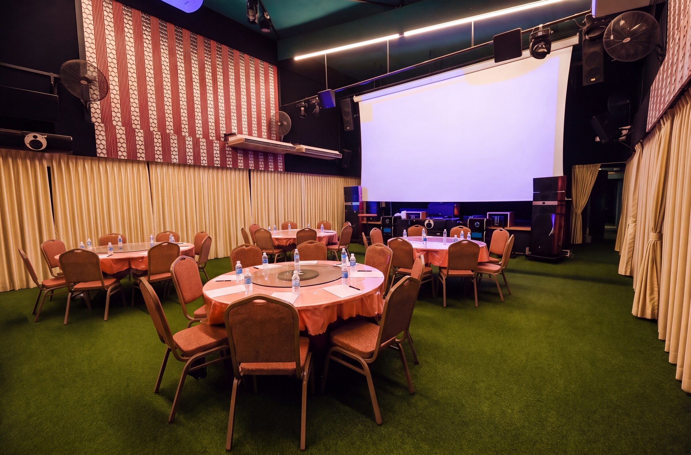 Emerald Hall in light mode — meeting setup with round tables, notepads and water, projection screen down
